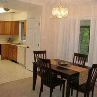 A cozy dining area with a view into the kitchen, featuring a wooden table and chairs under a chandelier.