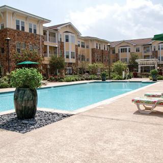 A residential apartment complex featuring an inviting outdoor swimming pool, surrounded by landscaped gardens and sun loungers.