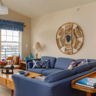 A cozy living room featuring a blue sofa, decorative pillows, wall art, and a sunlit window.