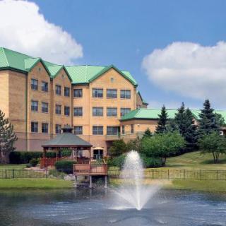 A building with a green roof overlooking a small lake with a fountain and surrounded by trees.
