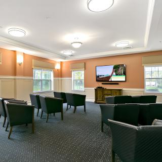 A comfortable meeting room with chairs arranged around a television and multiple windows providing natural light.