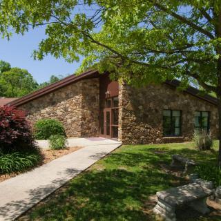 A stone building surrounded by lush greenery and trees on a sunny day.