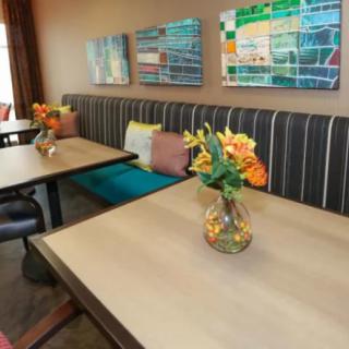 A cozy dining area with contemporary decor, featuring tables adorned with floral arrangements and colorful wall art.