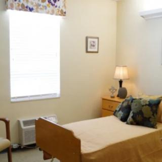 A cozy bedroom with a bed, lamp, chair, and window.