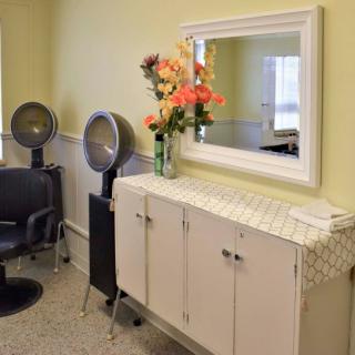 A well-organized salon corner with chairs, hairdryers, a mirror, and fresh flowers on the cabinet.