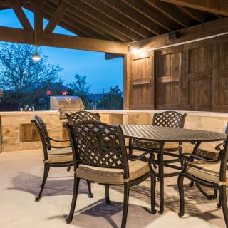 A cozy outdoor patio with a table and chairs under a covered structure, beautifully lit in the evening.