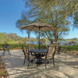 A tranquil outdoor patio set by the lake, featuring a table with chairs under an umbrella surrounded by lush trees.