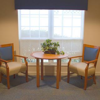 A cozy seating arrangement with two chairs and a table placed in front of a window, featuring a potted plant as a centerpiece.