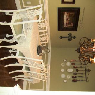A dining room featuring a white table with matching chairs and elegant wall decor, complemented by a chandelier.