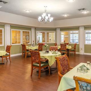 An elegant dining room with tables and chairs set for guests under a chandelier.