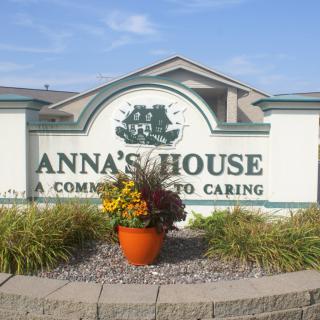 A sign for Anna's House, surrounded by landscaping and a flower arrangement.