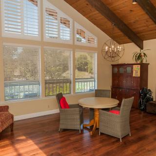 A cozy living room with large windows, wooden ceiling beams, and a small dining area.