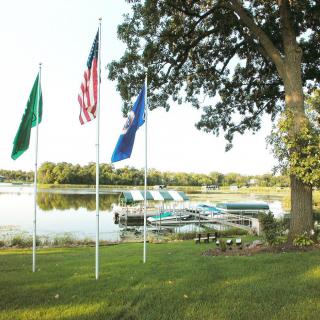 A scenic view of a lakeside dock with boats, surrounded by flags and trees.