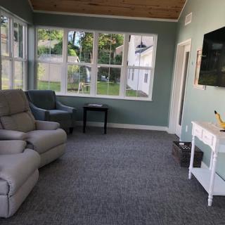 A cozy living room with large windows, comfortable seating, and a mounted TV.