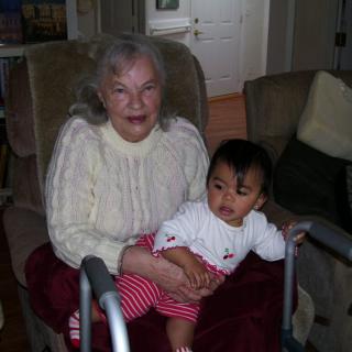 An elderly woman sitting in a chair holding a young child indoors.