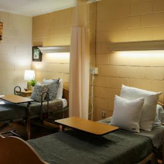 A well-lit patient room featuring two hospital beds with comfortable bedding.