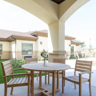 A sunny patio with wooden table and chairs in a garden setting.