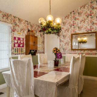 A cozy dining room with floral wallpaper, a chandelier, and a mirrored wall.
