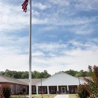 A building with an American flag in front, set against a blue sky with clouds.