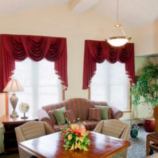 A cozy living room with a dining area, featuring red curtains, comfortable seating, and vibrant greenery.
