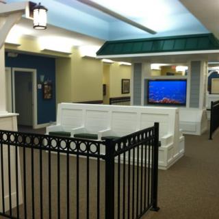 An indoor corridor with a decorative black fence, ceiling lights, and a TV screen mounted on the wall.