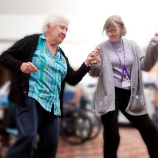 Two elderly women enjoying a dance together indoors.