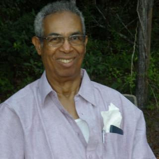 A man wearing a shirt and glasses smiles outdoors.
