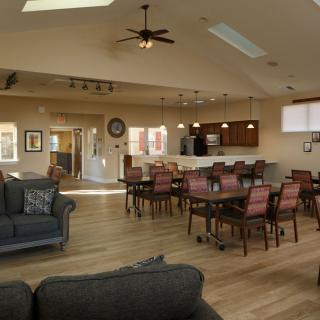 An open-concept living room with dining and kitchen areas, featuring comfortable furniture and wooden flooring.