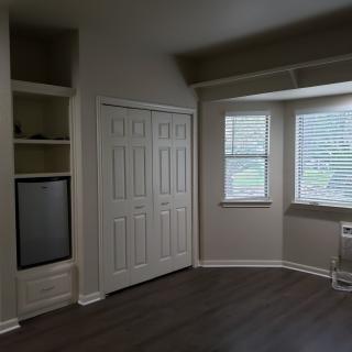 An empty room with built-in shelves and a closet, featuring large windows and wood flooring.