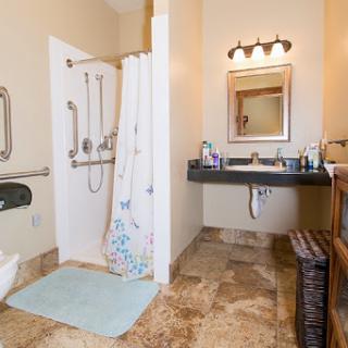 A spacious bathroom featuring a shower area, sink with mirror, and accessible amenities.