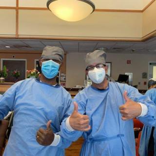 Healthcare workers celebrating teamwork with a thumbs-up gesture in surgical attire.