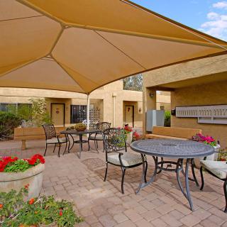 A cozy outdoor patio area with tables, chairs, and a shade canopy.