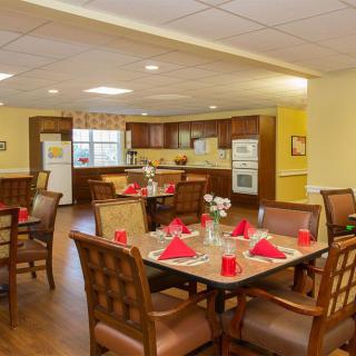 A cozy dining area with neatly set tables, featuring red napkins and a view of an adjacent kitchen.
