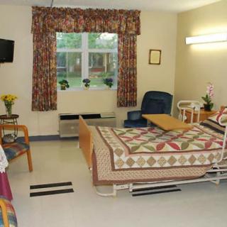 A well-furnished hospital room with a bed, chair, and window.