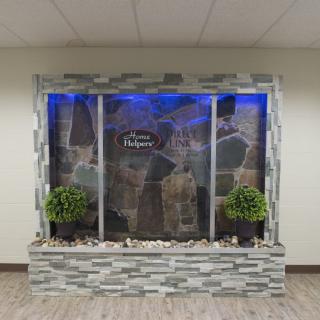 An indoor water feature with a stone wall design, accented by blue lighting and potted plants.