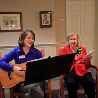 Two women performing music indoors, with one playing the guitar and both singing.