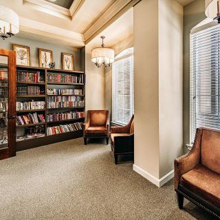 A cozy library corner featuring bookshelves filled with books, comfortable armchairs, and large windows allowing natural light.