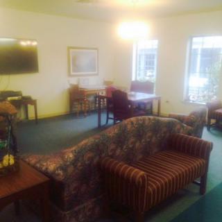 A cozy living room with a variety of seating options and a television, featuring large windows and carpeted flooring.