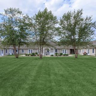 A row of residential buildings with a neatly maintained lawn and several trees in the foreground.