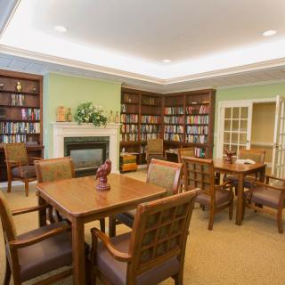 A cozy library room with wooden tables and chairs, surrounded by bookshelves and a fireplace.