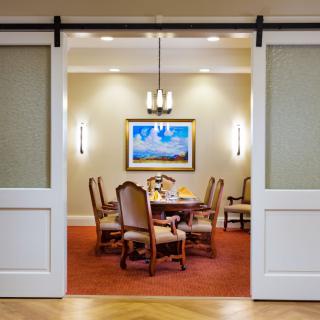 A well-decorated dining room with a table and chairs, illuminated by a chandelier and complemented by artwork on the wall.