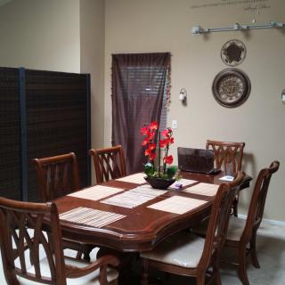 A dining room with a wooden table and chairs, featuring decorative wall art and a centerpiece of red flowers.