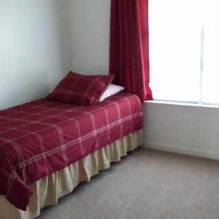 A minimalist bedroom with a single bed featuring red bedding and matching curtains beside a large window.