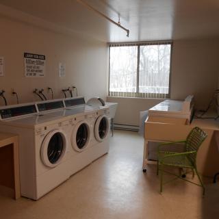 A laundry room with washing machines and dryers near a window.