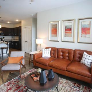 A modern living room with a brown leather sofa, abstract artwork, and an open kitchen layout.