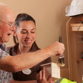 An elderly man and a young woman collaborate on a painting project.