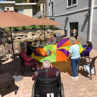 Seniors enjoying an outdoor group activity with a colorful parachute under a parasol.