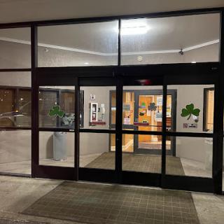 Entrance of a building at night, featuring glass doors and soft indoor lighting.