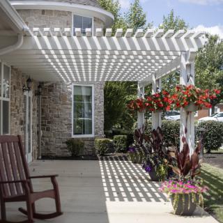 A serene outdoor patio with a pergola providing shade, adorned with hanging flower pots and a wooden chair.
