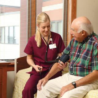 A nurse checks the blood pressure of an elderly man in a hospital room.